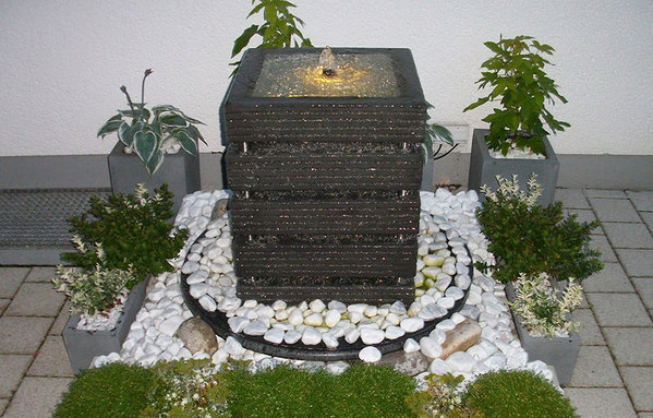 Beleuchteter Gartenbrunnen in anthrazit umgeben von weißen Kieselsteinen.\\n\\n20.10.2017 12:14